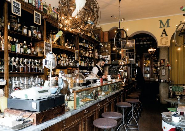 Interni del MAG Cafè, bar di Flavio Angiolillo a Milano. Bancone, scaffali di liquori, lampade design.