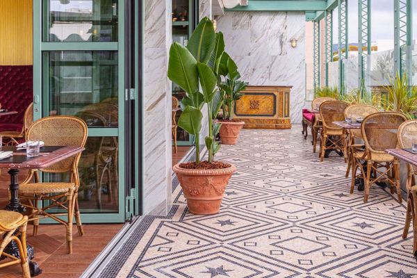 Interni Gucci Osteria: tavoli rattan, pavimenti decorati, piante. Food e fashion brand experience.