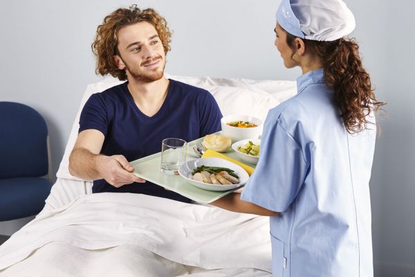 CIRFOOD: Ristorazione collettiva solidale. Infermiera serve pasto a paziente in ospedale.