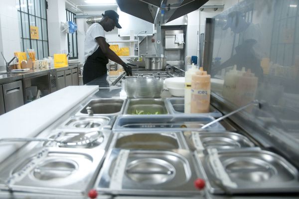 Glovo Cook Room Milano: cuoco al lavoro in cucina professionale. Ingredienti freschi e attrezzature in acciaio inox.
