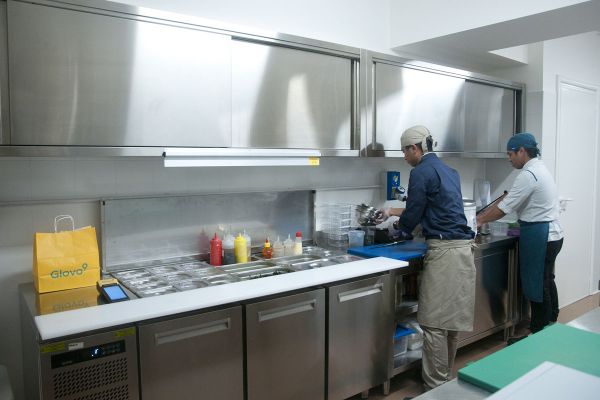 Glovo Cook Room Milano: chef al lavoro in cucina professionale. Borsa Glovo visibile.