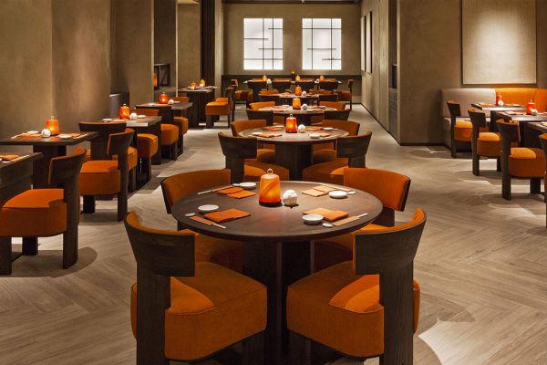 Interni del ristorante Nobu Milano, parte dell'impero Armani. Tavoli rotondi e sedie arancioni.