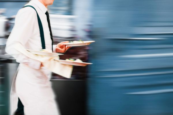 Foodservice: cameriere in movimento con piatti. Lentezza e velocità nel settore ristorazione.