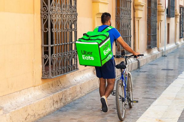 Consegna Uber Eats: rider in bici con zaino termico verde. Servizio di food delivery a domicilio.