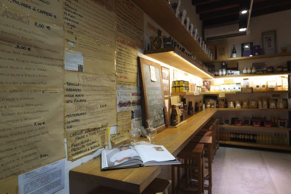 Interno di INO Firenze: gastronomia, filiera alimentare. Menù artigianale, scaffali con prodotti tipici. Alessandro Frassica e la cucina toscana.