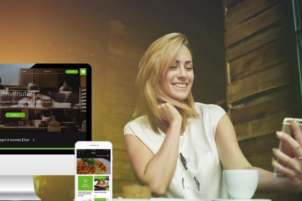 Box delivery Elior: donna sorridente con smartphone, app e sito web per ordinare cibo a domicilio.