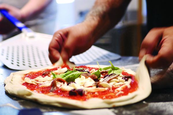 Pizza napoletana fresca in preparazione. Ingredienti: pomodoro, mozzarella, alici, olive, basilico. Tradizione culinaria.
