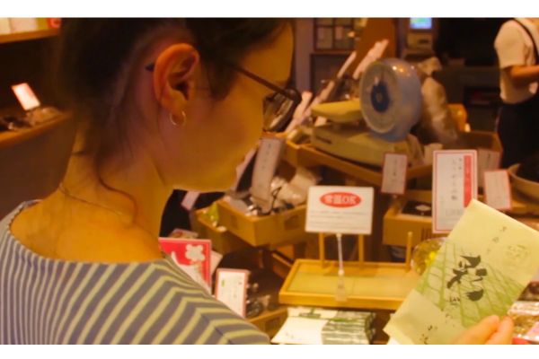 Tour virtuale cibo: donna guarda confezione prodotto tipico giapponese. Robot e video per storytelling alimentare.