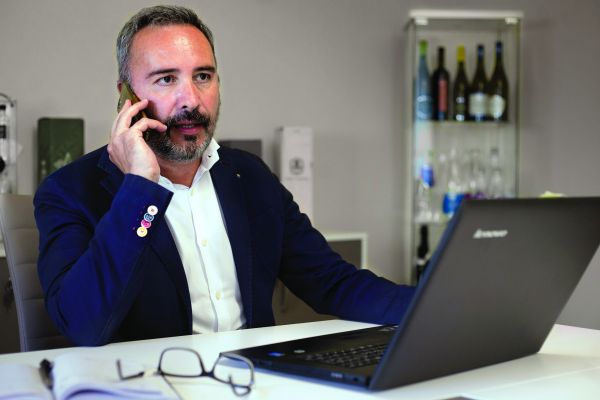 Grossista bevande al telefono con laptop. Dilemma ampliamento offerta. Bottiglie di vino sullo sfondo.