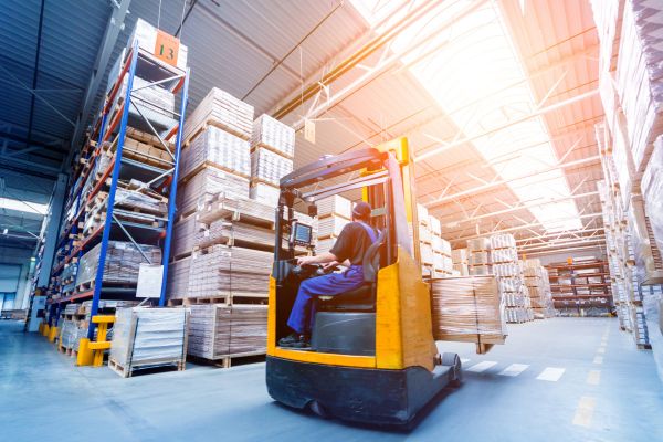 Magazzino grossisti: carrello elevatore con operatore. Scaffali pieni di merce per industria e fuori casa.