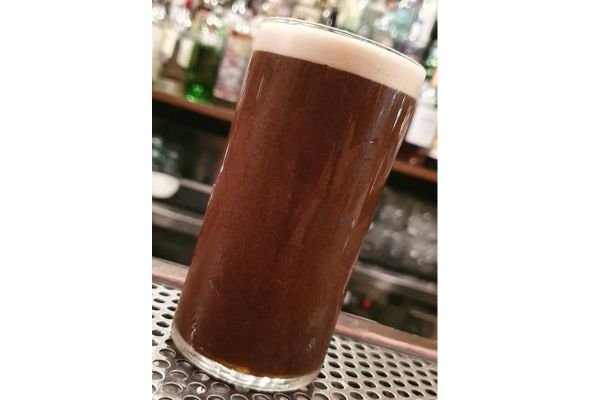 Cocktail di birra scura in bicchiere alto con schiuma bianca. Drink per la giornata mondiale della birra.