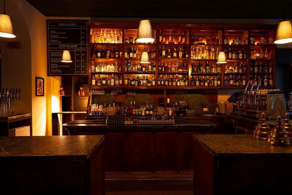 Interno del Caffè della Pusterla. Bar con scaffali di liquori e cocktail, illuminazione soffusa. Flavio Angiolillo.