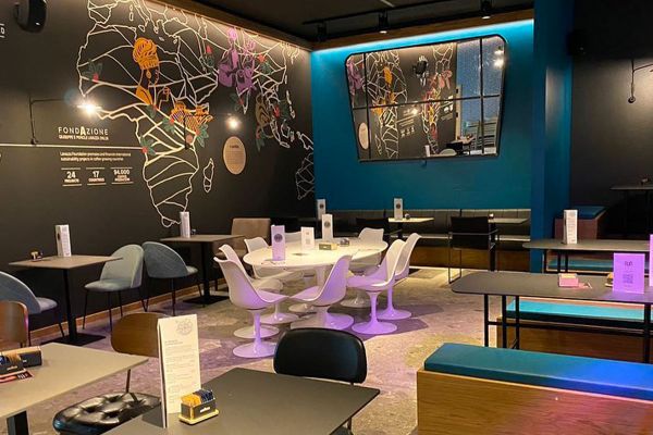 Interno del Gūd Bocconi: tavoli, sedie design, mappa del mondo decorativa. Mensa universitaria innovativa.