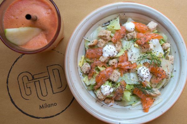 Insalata Gūd con salmone, mozzarella e crostini. Accanto, succo di frutta. Ristorante Gūd a Milano, vicino Bocconi.