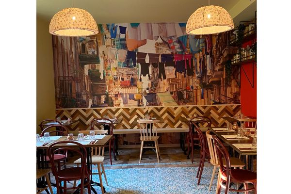 Interno di Pizzium Parma: tavoli apparecchiati, sedie in legno, lampade floreali e carta da parati con panni stesi.