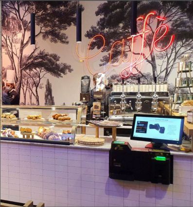 Pagamenti automatici nel locale del futuro Costa Group. Bar con cassa automatica e insegna Cafe al neon.