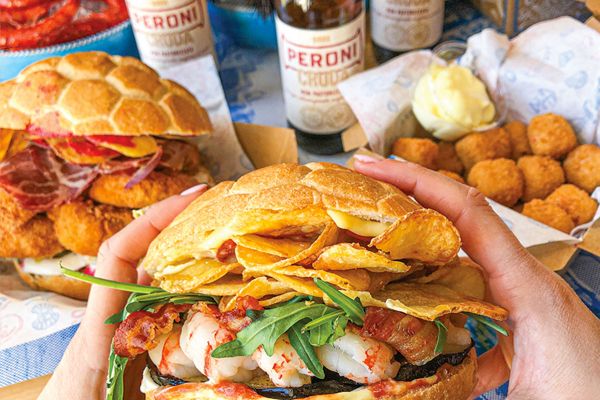 Panini di mare Pescaria a Roma. Primo piano su panino gourmet con gamberi, patatine e Peroni.