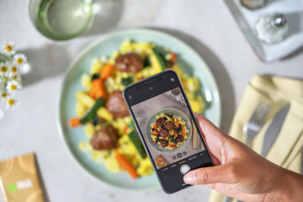 Nuovi consumi italiani: foto con smartphone di piatto HelloFresh con polpette e verdure.