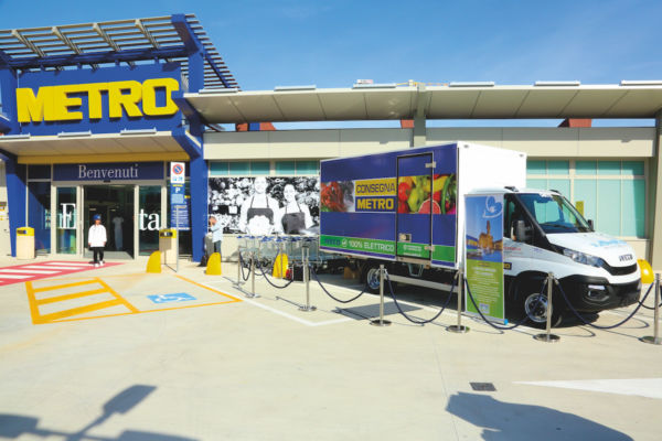 Furgone elettrico Metro per la consegna. Focus su Pl, localismo e delivery. Negozio Metro sullo sfondo.