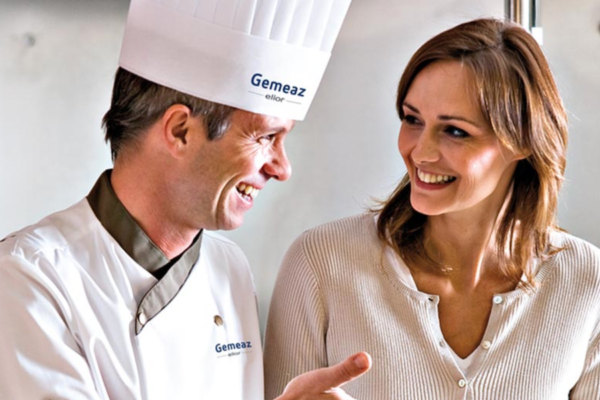 Chef Gemeaz Elior Ristorazione sorride a cliente. Fusione aziendale, ristorazione collettiva.