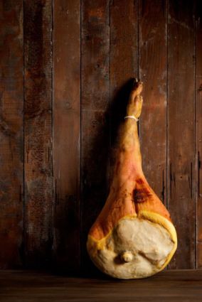 Prosciutto di San Daniele DOP appeso su sfondo rustico in legno. Salumi italiani.