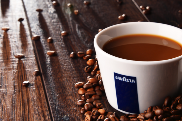 Tazza di caffè Lavazza con chicchi su legno. Ricavi record Lavazza Group.