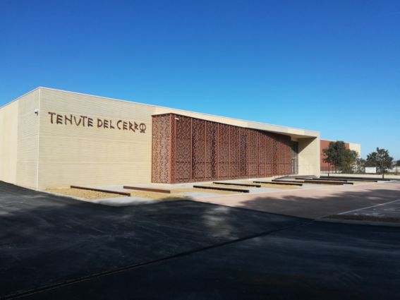 Nuova cantina Unipol per Tenute del Cerro. Architettura moderna, facciata beige con griglia decorativa. Cielo azzurro.