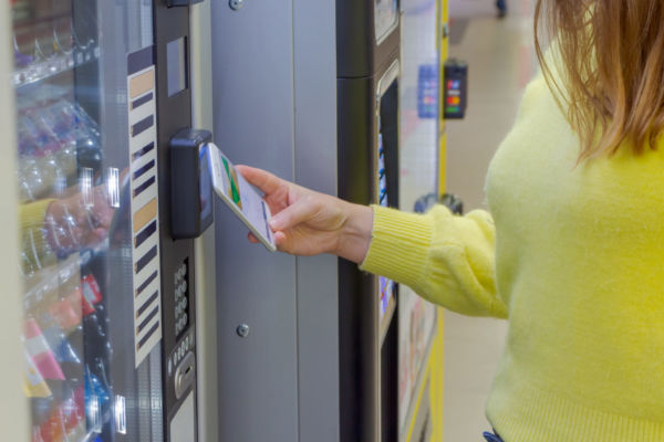 Venditalia: donna usa smartphone a distributore automatico. Pagamento contactless.