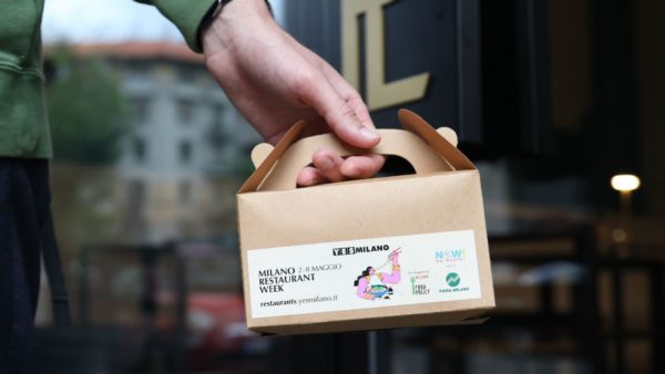 Doggy bag Milano Restaurant Week. Mano che tiene scatola take away. Ristoranti Milano contro lo spreco alimentare.