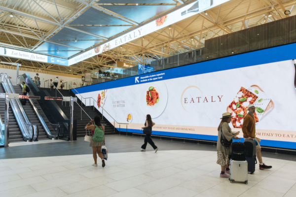 Eataly Autogrill a Fiumicino: negozio con pizza, pasta e prodotti tipici italiani in aeroporto. Viaggiatori e scale mobili.