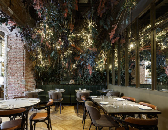 Interno Quore Italiano Milano: design con piante, luci, tavoli apparecchiati e mattoni a vista.