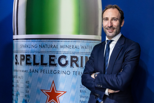 Uomo in giacca blu con bottiglia Sanpellegrino. Fatturato Sanpellegrino 2021. Acqua minerale frizzante Sanpellegrino.