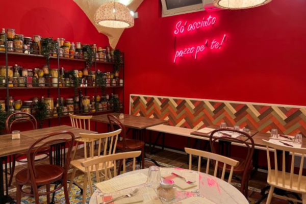 Interni di PIZZIUM Vomero, Napoli. Tavoli in legno, scaffali con conserve e scritta al neon.