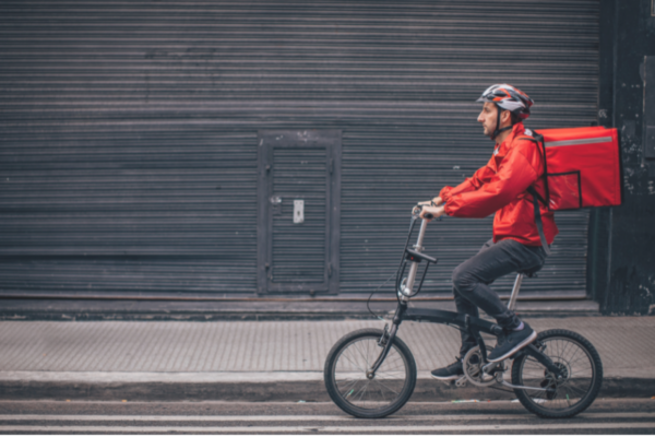 Consegne post pandemia: rider in bici con zaino termico rosso. Ordini digitali resistono.