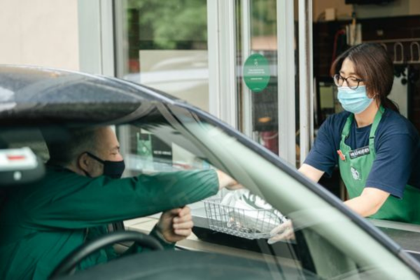Starbucks drive-thru: barista consegna ordine a cliente in auto. Servizio off premises.
