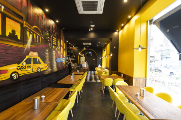 Interni del ristorante A 3 Strati a Milano. Arredamento giallo, murales taxi NYC.