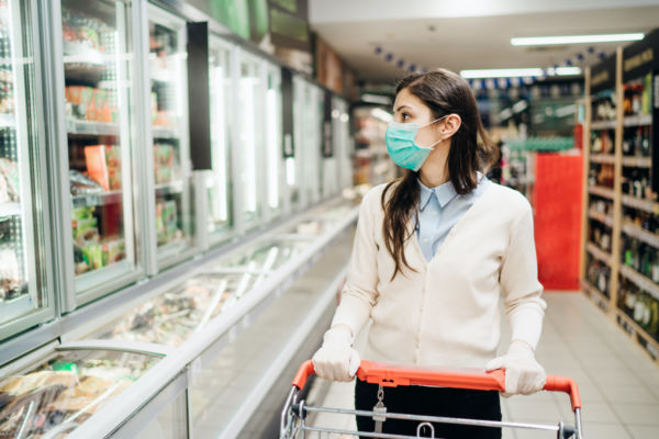 Donna con mascherina al supermercato, reparto surgelati. Acquisti alimentari.