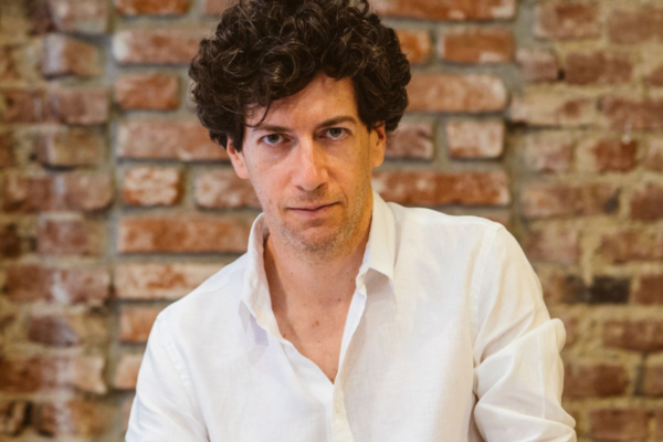 Ritratto del fondatore di Pizzium, con camicia bianca e capelli ricci, sullo sfondo un muro di mattoni.