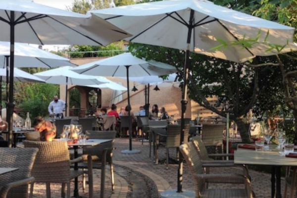 Dehors ristorante: tavoli all'aperto con ombrelloni bianchi e sedie in vimini. Spazio pubblico accogliente.