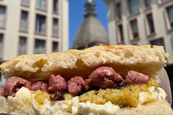 Panino gourmet All'Antico Vinaio a Torino, con salsiccia e crema. Specialità toscana in primo piano, Mole sullo sfondo.