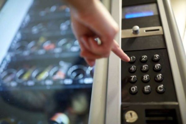 Mano preme pulsante su distributore automatico. Snack e bevande disponibili.