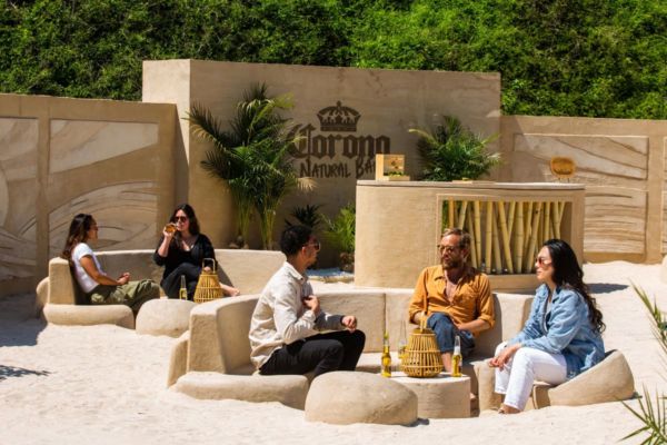 Apertura Corona Natural Bar: persone rilassate sulla spiaggia con birra Corona. Divertimento eco-friendly.