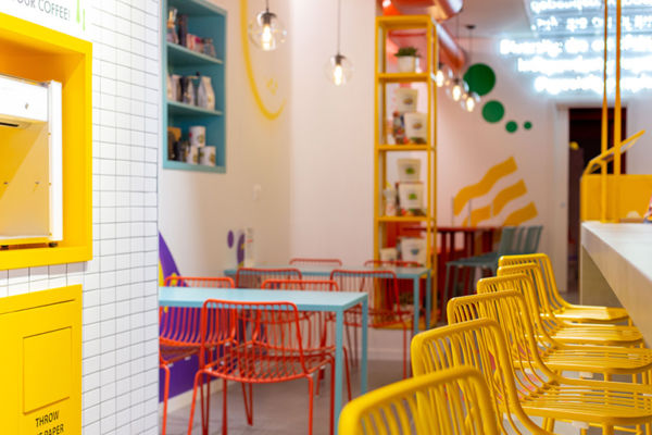 Interni colorati di Fluid, nuova caffetteria: sedie gialle, tavoli azzurri, scaffali. Design moderno e accogliente.