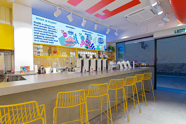 Interni moderni di Fluid: caffetteria con bancone, sedie gialle e menù luminoso. Design accogliente per caffè e cibo gustoso.