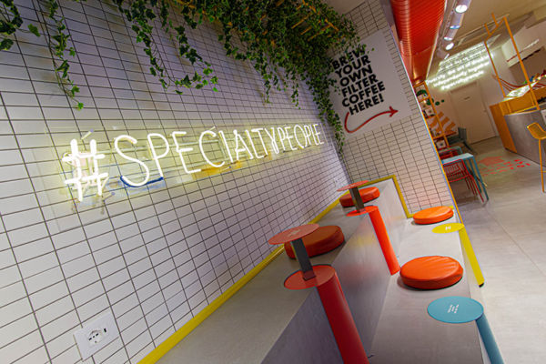 Interni moderni di Fluid caffetteria: neon #specialtypeople, sedute colorate, piastrelle bianche.