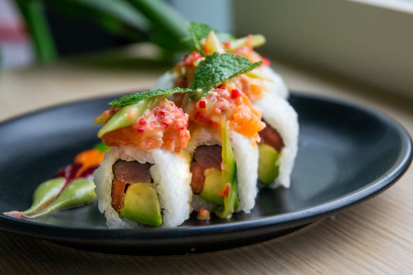 Roll ALMAKI: sushi con avocado, tonno e salmone su piatto nero. Cucina fusion.