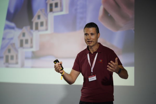 Relatore parla di digitalizzazione Horeca. Case stilizzate sullo schermo. Automazione settore alberghiero.