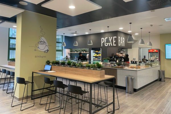 Bocconi 12, food court Pellegrini: angolo poke bar. Tavoli alti con sgabelli, design moderno.
