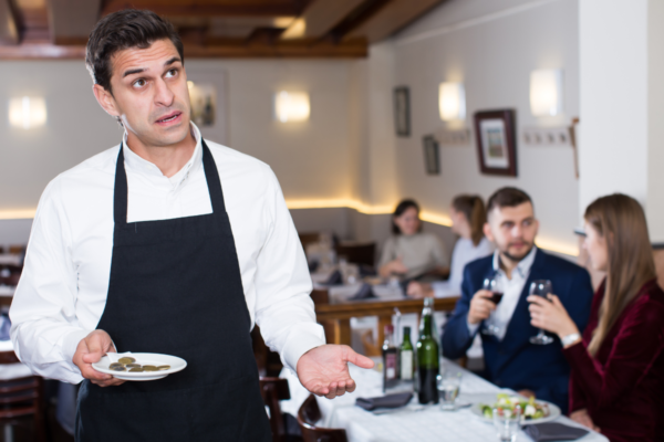 Crollo mance post Covid USA: cameriere deluso con poche monete in un ristorante.
