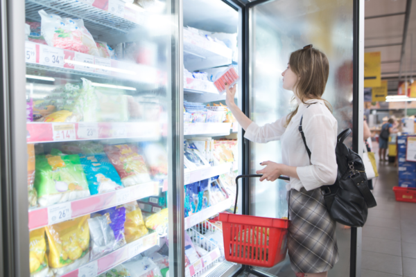 Donna al supermercato sceglie surgelati plant based. Frigorifero pieno di prodotti Impossible Foods.